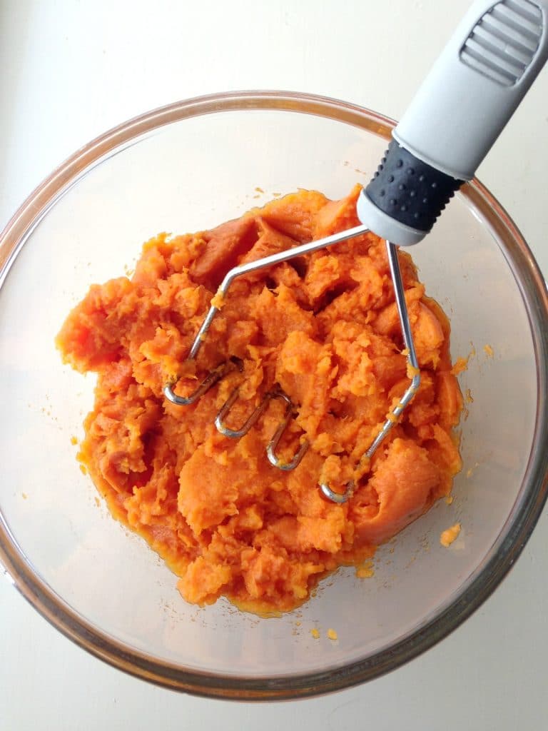 Baked sweet potatoes being mashed with a hand masher